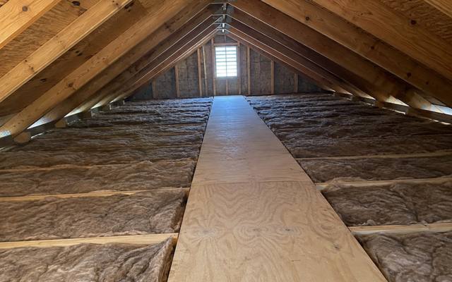 Long attic with insulation batts on both sides of a plywood walkway leading to a gable vent