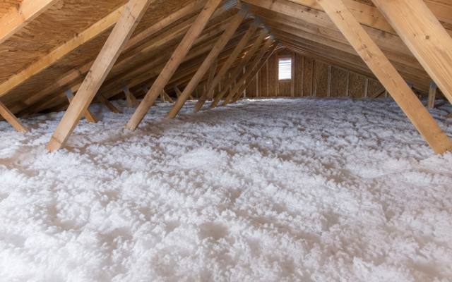 White blown fiberglass insulation spread across an attic floor between angled roof trusses
