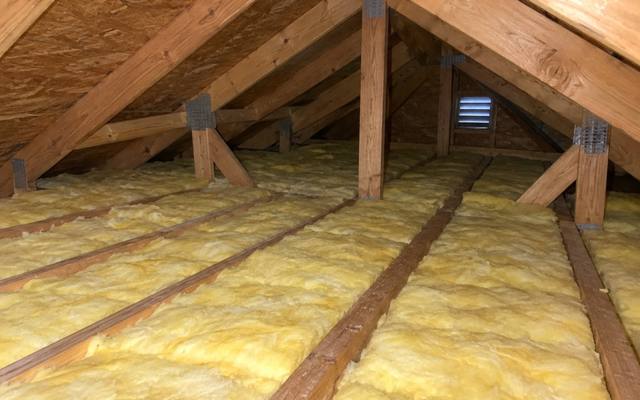 Yellow fiberglass batts laid between attic joists with a louvred gable vent at the far end of the attic