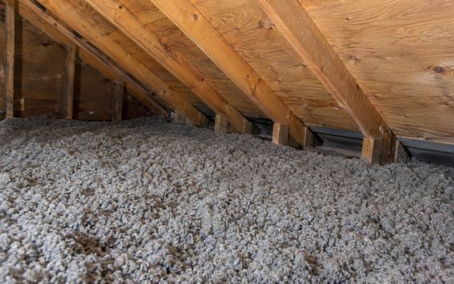 Deep, even layer of grey blown insulation running to the low eaves of an attic with vent openings under the roof edge